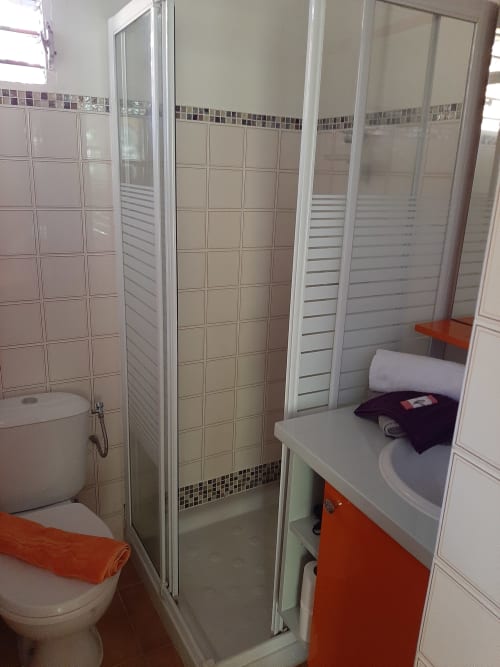 Modern bathroom with shower enclosure, toilet, and vanity with red cabinet at Residence de Vacances Mon Refuge, Martinique