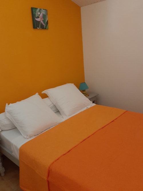 Bright orange and white bedroom at Residence de Vacances Mon Refuge in Les Anses d'Arlet with white pillows and orange