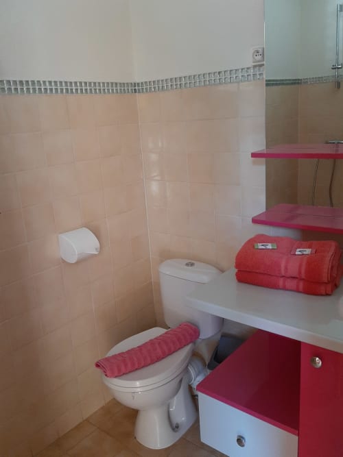Bathroom with white toilet, pink tile walls, red towels and shelves at Residence de Vacances Mon Refuge, Les Anses d'Arlet