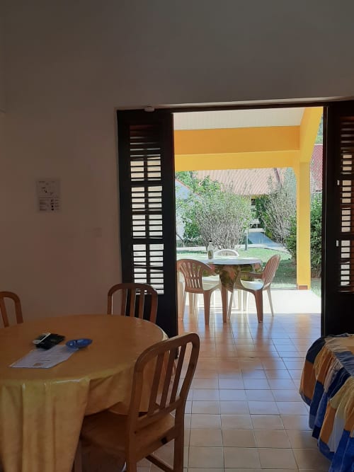 Dining area with round table opening to yellow-roofed patio, garden views at Mon Refuge, Martinique