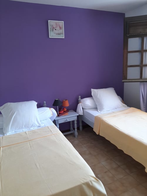 Chambre violette avec deux lits jumeaux, oreillers blancs et table de nuit avec lampes à l'hôtel Mon Refuge, Martinique