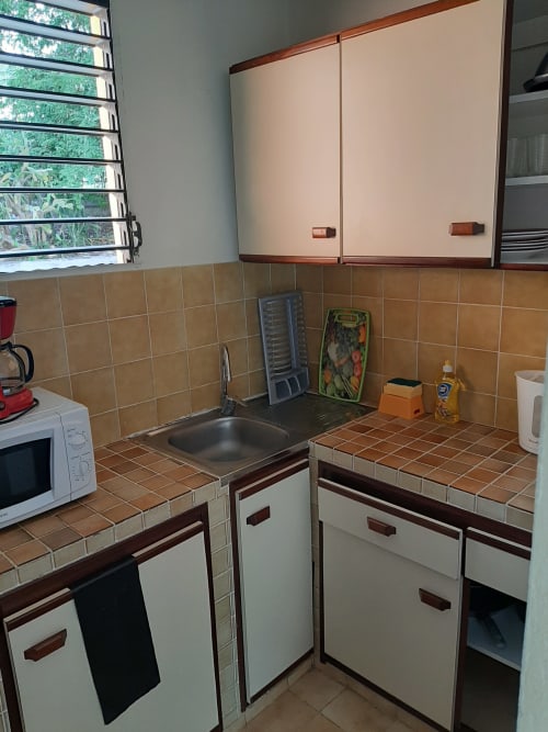 Petite cuisine de l'appartement à la Résidence de Vacances Mon Refuge avec armoires crème, plan de travail et crédence en carrelage brun