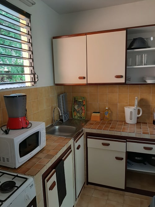 Cuisine compacte avec crédence en carrelage terre cuite, meubles crème, micro-ondes et évier à la Résidence de Vacances Mon Refuge