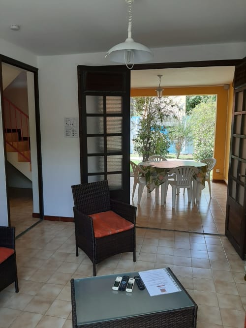 Séjour lumineux avec vue sur jardin, mobilier en rotin aux coussins rouges, table à manger et accès à terrasse