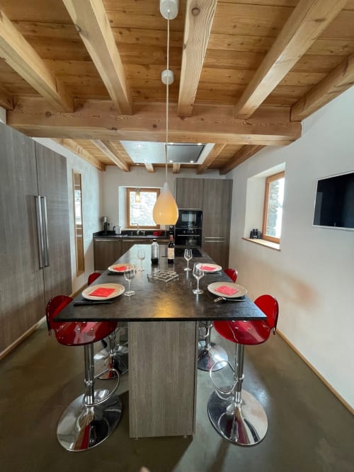 Cuisine ouverte moderne et salle à manger dans chalet Tignes avec poutres bois apparentes, îlot noir, tabourets rouges, et