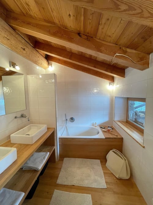 Salle de bain rustique aux poutres apparentes du Chalet Du Sarrasin à Tignes avec double vasques, baignoire et carrelage blanc