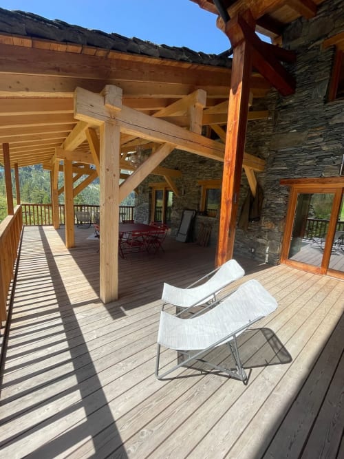 Terrasse en bois avec transats au Chalet Du Sarrasin, Tignes. Bâtisse en pierre, poutres apparentes et vue montagne.