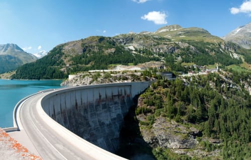 Barrage moderne courbé surplombant un lac alpin turquoise entouré de montagnes et forêts près de Tignes, France