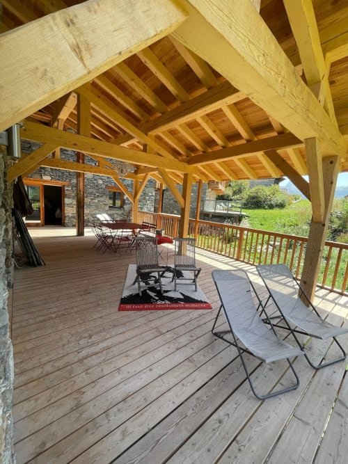 Terrasse en bois avec transats sous une pergola en bois au Chalet Du Sarrasin, Tignes. Bâtiment en pierre et vue alpine.