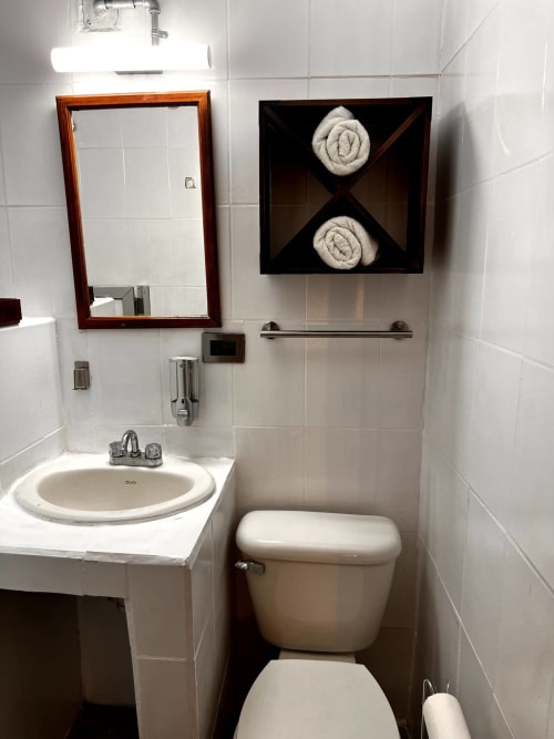 Baño limpio del Hotel Boutique BajaReal en La Paz con lavamanos, inodoro, espejo y almacenamiento de toallas
