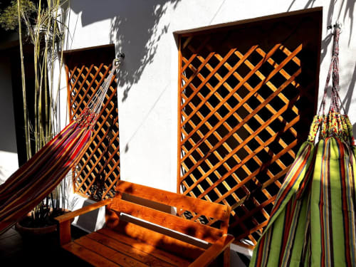 Soleado patio del Hotel Boutique BajaReal en La Paz con paneles de celosía de madera, coloridas hamacas y macetas que proyectan sombras