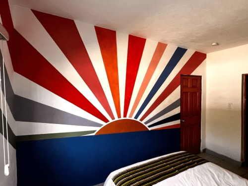 Mural del amanecer en la habitación del hotel La Paz con rayos coloridos sobre horizonte azul marino y cama blanca