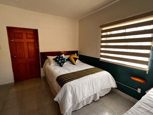 Habitación del Hotel Boutique BajaReal en La Paz con cama doble, ropa de cama a rayas, cojines decorativos, puerta roja y ventana a rayas