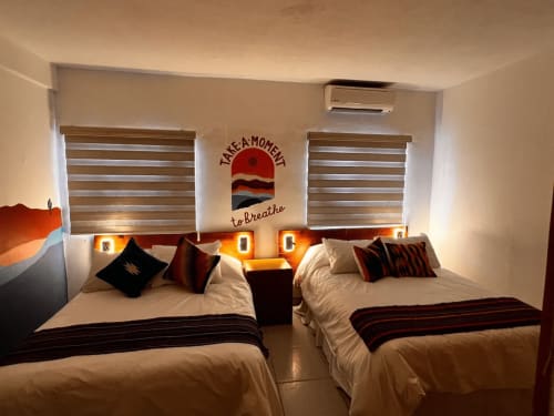 Camas gemelas con almohadas decorativas en habitación de hotel en La Paz, con arte mural inspirado en atardecer e iluminación ambiental