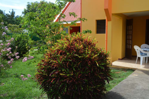 Colorful garden at Mon Refuge vacation residence in Martinique with yellow building, red flowers, and white patio furniture