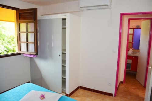 Chambre lumineuse à la Résidence de Vacances Mon Refuge avec lit bleu, encadrement de porte rose, fenêtre avec vue sur le jardin