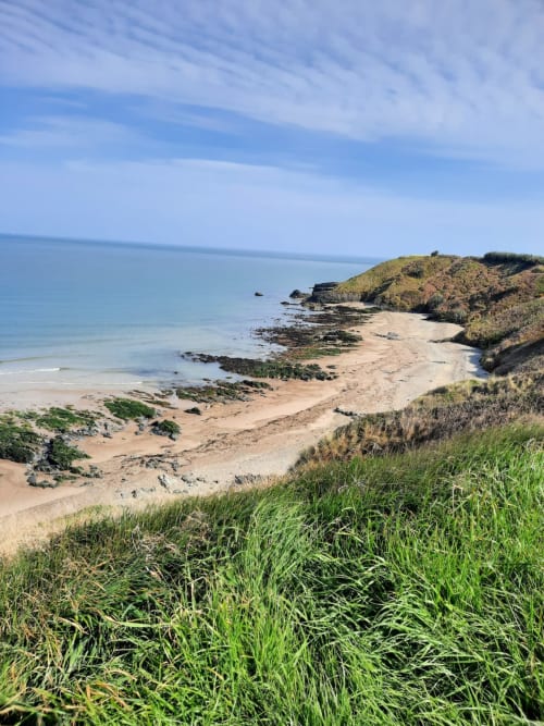Coastal beach view from Hilltop Seaview Apartment in Wicklow with sandy shores, rocky outcrops, and green cliffs