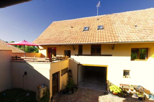 Façade du gîte La Grange à Neuf-Brisach : toit aux tuiles jaunes, murs crème, balcon et allée