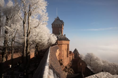 Des arbres givrés encadrent la tour du château médiéval en briques rouges sous la neige à Neuf-Brisach, France
