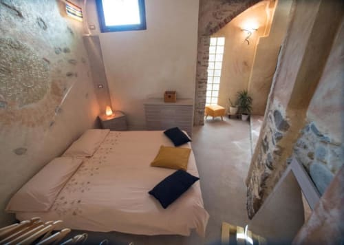 Camera wellness CasaRosada a Vidracco con muri in pietra, letto bianco, cuscino giallo, illuminazione d'atmosfera e accesso alla vista giardino