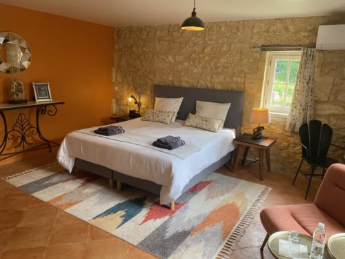 Élégante chambre au Château Haut Clarise avec murs en pierre, accents orange et vue sur le jardin