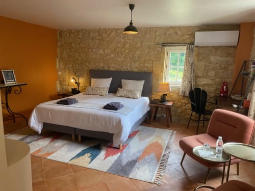 Chambre spacieuse au Château Haut Clarise avec lit blanc, murs orange, éléments en pierre et vue sur le jardin