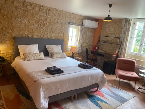 Chambre spacieuse au Château Haut Clarise avec murs en pierre, lit double, climatisation, bureau et vue sur le jardin