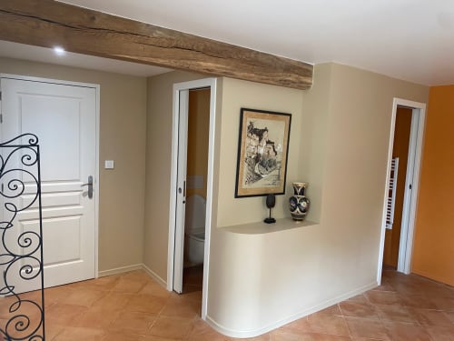 Couloir du Château Haut Clarise B&B avec poutre apparente, portes blanches, carrelage en terre cuite et alcôve décorée d'œuvres d'art