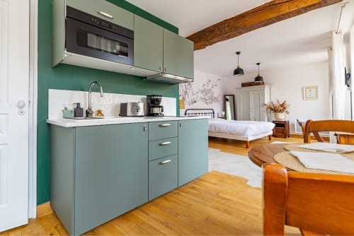 Modern studio apartment at La Maison George in Flavigny with sage green kitchenette, wooden beams, and bedroom visible in