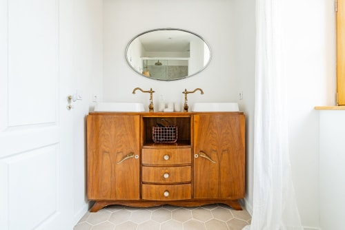 Salle de bains avec doubles vasques, robinetterie en laiton, meubles en bois et miroir ovale à La Maison George