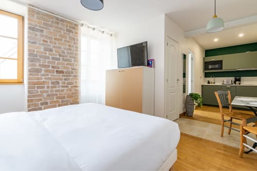 Chambre Logis Edith à La Maison George avec lit queen-size, murs en brique apparente, TV écran plat et kitchenette ouverte