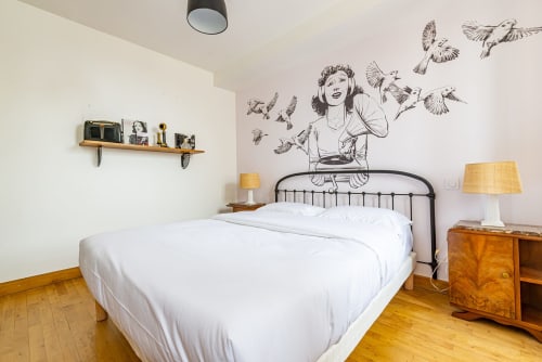 Chambre douillette à La Maison George avec literie blanche, décor vintage, mobilier en bois et fresque murale artistique d'une femme