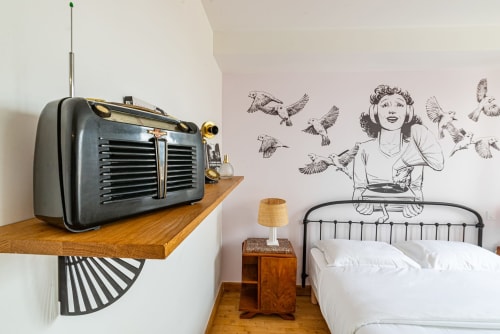 Poste de radio vintage sur étagère en bois au-dessus du lit avec tableau mural d'une femme et oiseaux à l'appartement Logis Edith de La Maison George