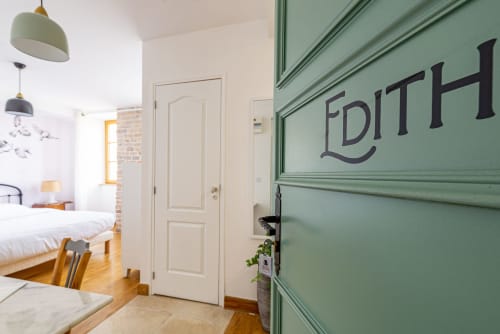 Entrée de l'appartement Logis Edith à La Maison George avec porte verte, luminaires design et vue sur la chambre