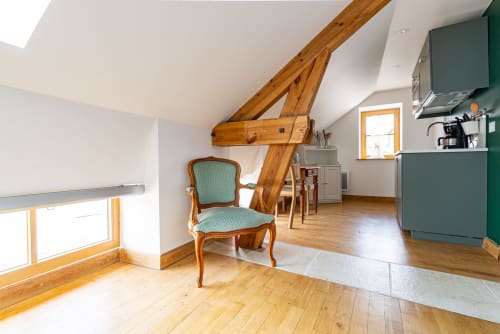Logis Olympe apartment at La Maison George with wooden beams, turquoise chair, and green kitchen