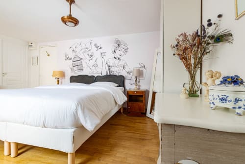 Logis Olympe bedroom at La Maison George with white bedding, sketch mural, dried flowers, and wooden floors