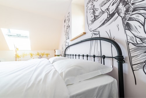 Modern bedroom with white bedding, black metal bed frame, and artistic mural at La Maison George, Flavigny sur Ozerain