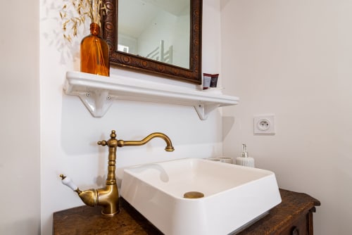 Elegant bathroom in Logis Marie at La Maison George with white rectangular sink, brass faucet, and framed mirror above white
