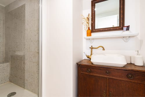 Elegant bathroom at La Maison George with vintage wooden vanity, brass faucet, mirror, and walk-in shower