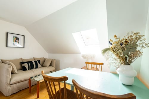 Lumineux studio sous les toits à La Maison George : canapé beige, table en bois, verrière, fleurs séchées et touches de menthe