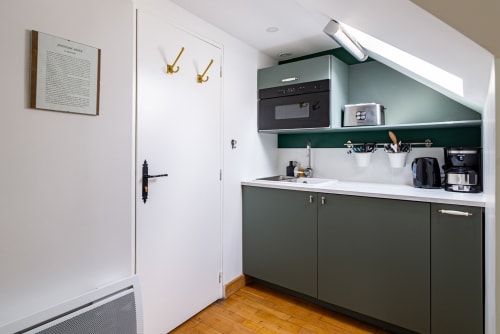 Kitchenette moderne à l'appartement Logis Joséphine de La Maison George avec meubles verts, plan de travail blanc et électroménager intégré