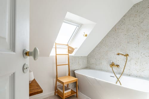 Salle de bain lumineuse à La Maison George avec puits de lumière, baignoire blanche, carrelage crème et échelle à serviettes en bois