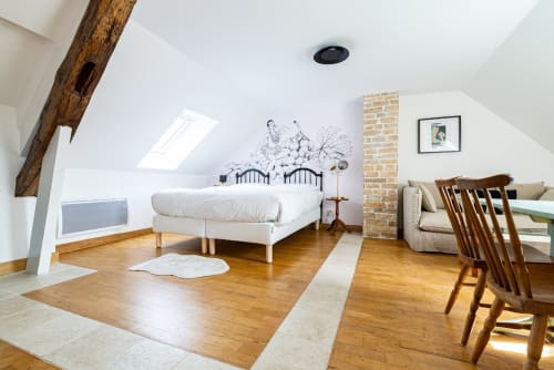 Chambre spacieuse du loft à La Maison George avec lit blanc, poutre apparente, cheminée en brique et chaises de salle à manger en bois