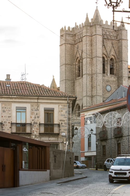 Torre de la catedral medieval y edificios históricos de piedra en la plaza del casco antiguo de Ávila con coches aparcados