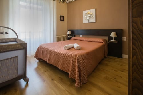 Spacious bedroom at Apartamentos Turísticos Ávila with orange bedspread, black headboard, twin lamps, and wooden floors