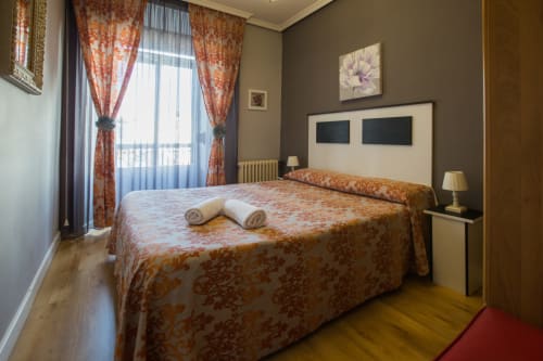 Bright bedroom at Apartamentos Turísticos Ávila with orange patterned bedding, balcony view, and modern amenities