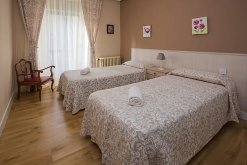 Twin bedroom with patterned bedspreads at Apartamentos Turísticos Ávila, featuring wooden floors and city views from balcony