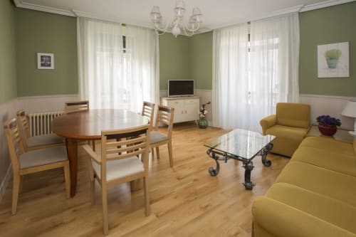 Bright apartment living space in Ávila with green walls, dining table, yellow sofa, TV, and balcony doors