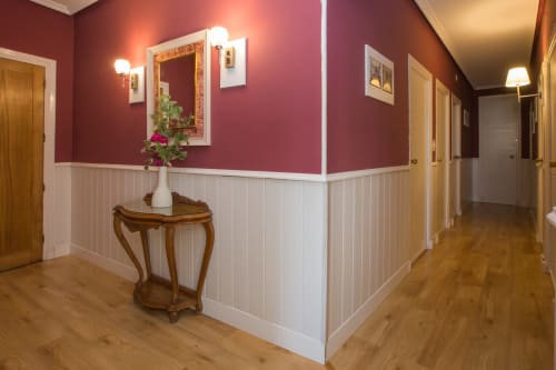 Elegant hallway in Ávila apartment with burgundy walls, white paneling, wooden doors, and mirror with sconce lighting