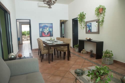 Área de comedor de Cozy House Downtown Cancun con mesa de madera, sillas de mimbre, plantas en macetas y obra de arte azul